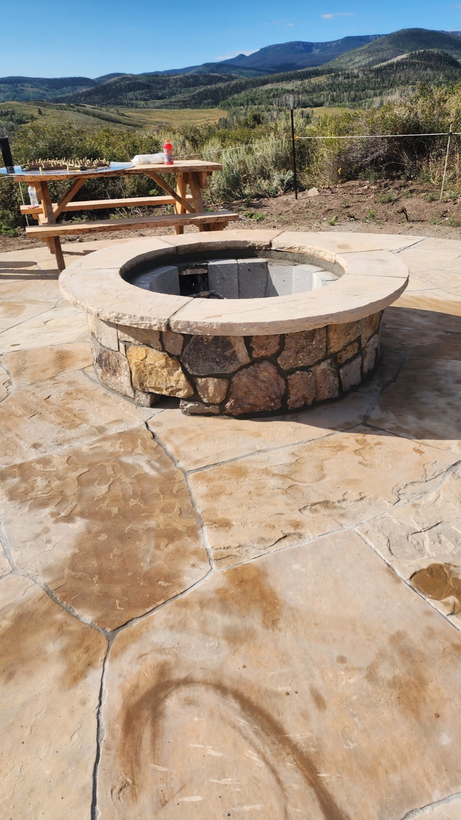 Round stone fire pit on a flagstone patio with a mountain valley view