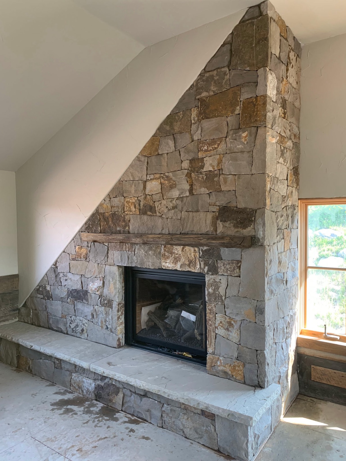 Full-height squared-stone fireplace with reclaimed timber mantel in a vaulted great room
