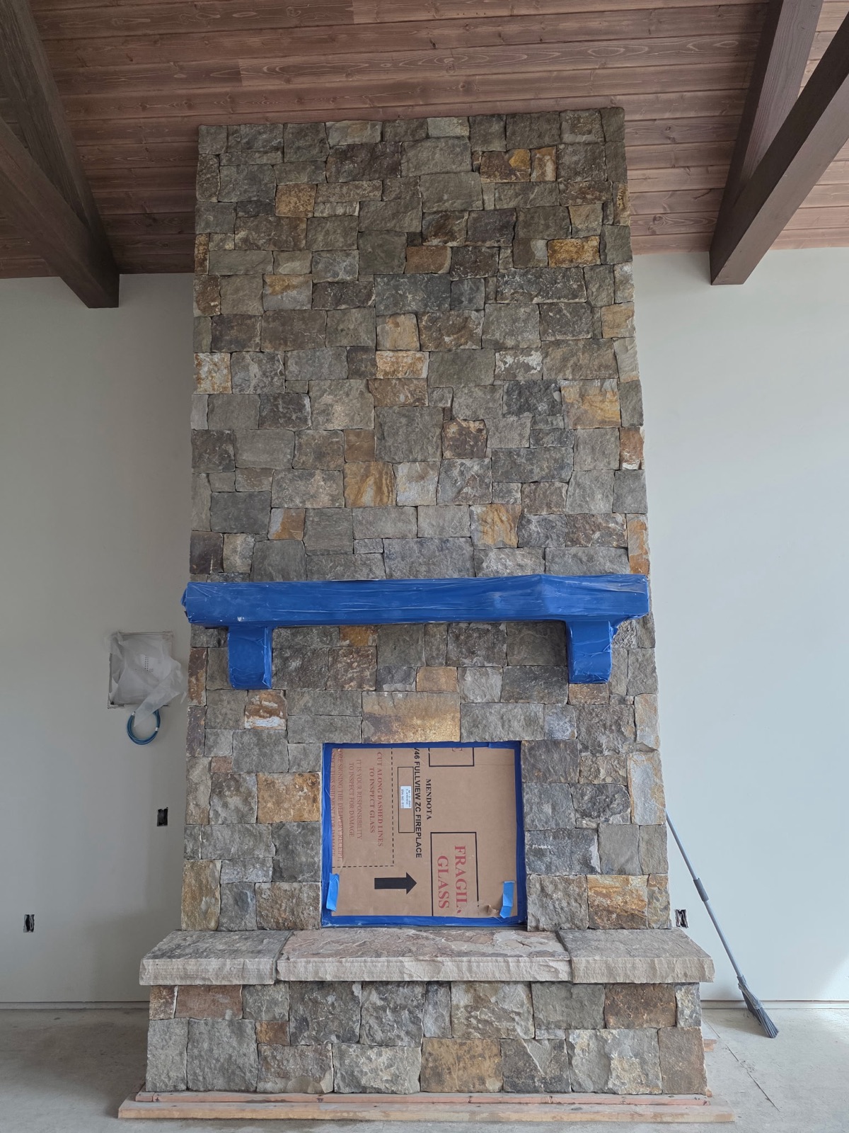 Floor-to-ceiling squared-stone fireplace with raised stone hearth, mid-install