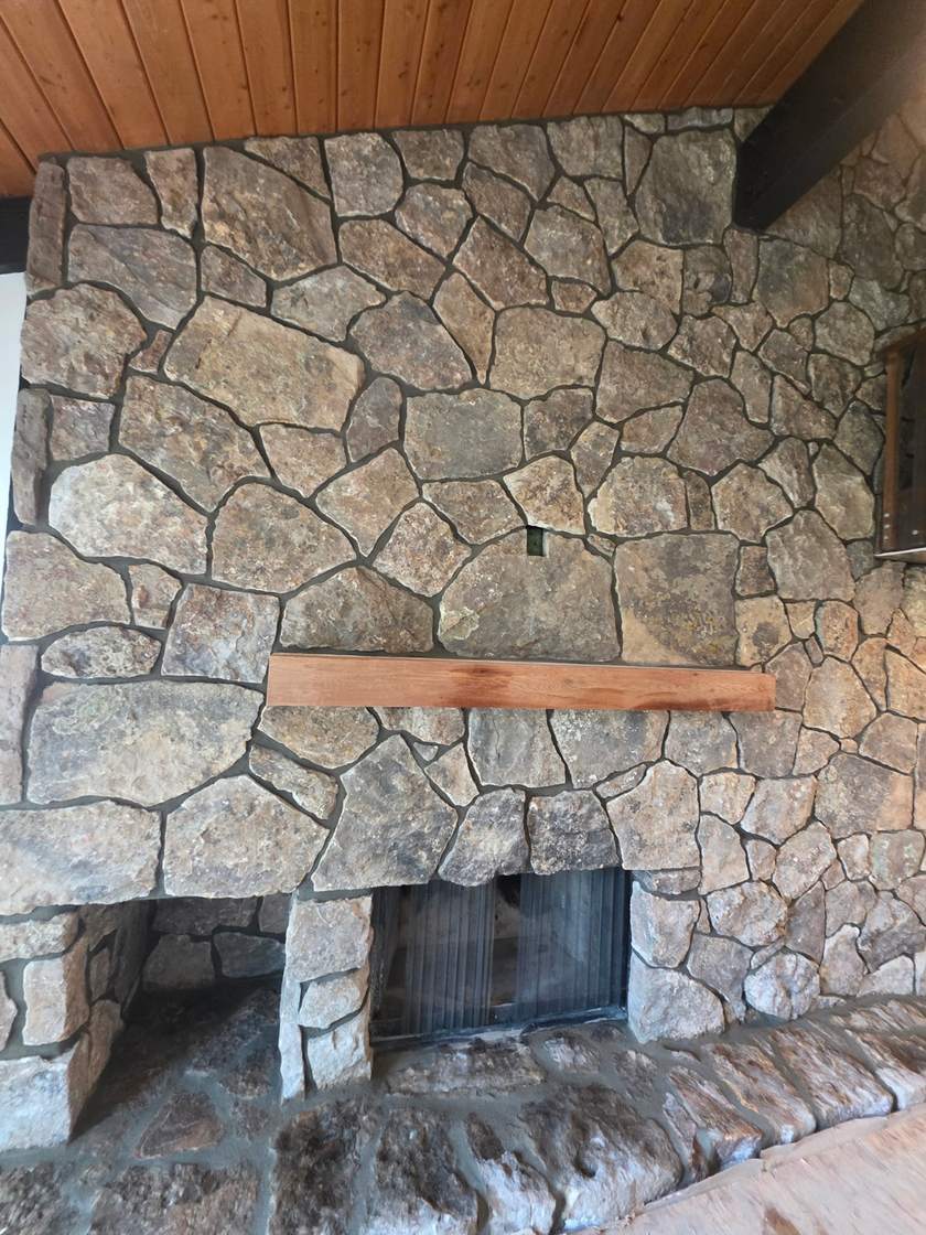 Moss-rock stone fireplace with timber mantel in a log home great room